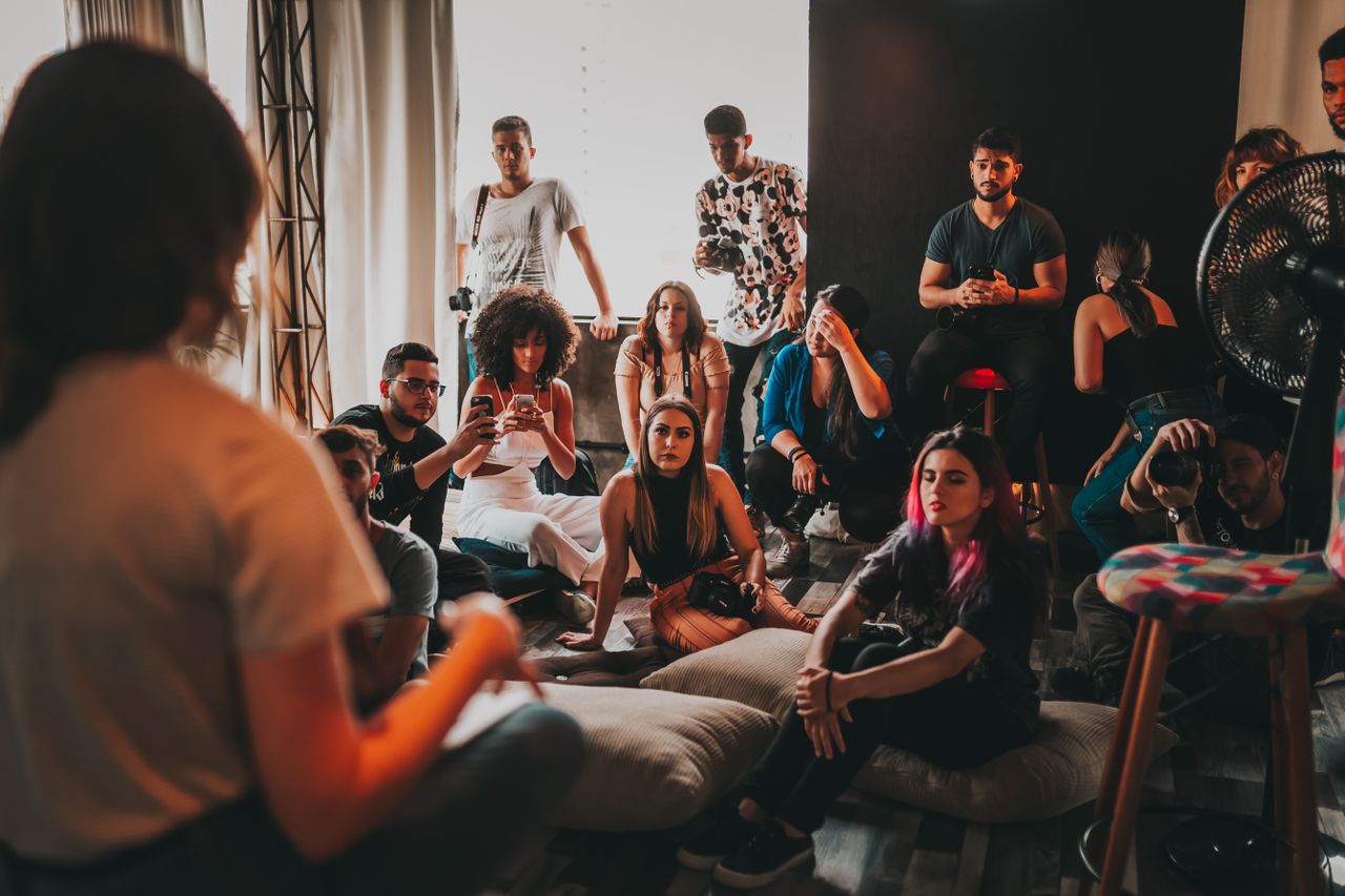 Group of attentive young multiracial community members in casual outfits meeting in modern studio and listening to female speaker sitting on mat